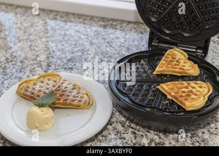 Deliziosi waffle a forma di cuore preparati con gelato dolce alla vaniglia e guarniti con balsamo al limone Foto Stock