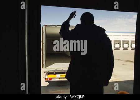 Il lavoratore agita la mano, guidando il conducente del carrello quando entra nell'hangar. Trasporto e carico di merci. Foto Stock