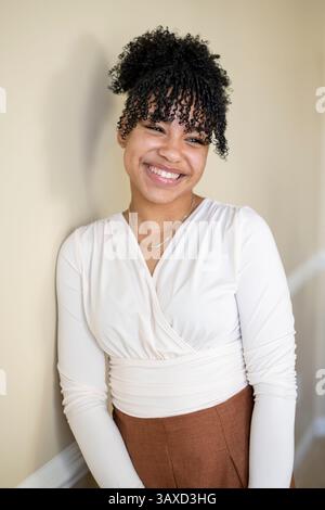 Donna sorridente in camicetta bianca si appoggia casualmente contro il muro Foto Stock
