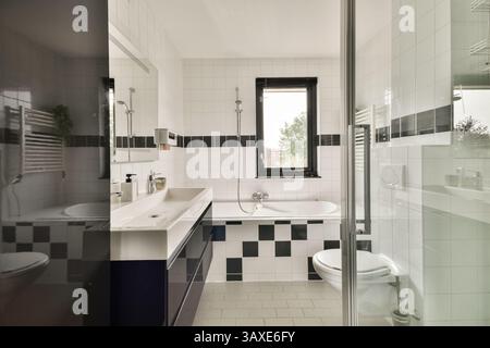 Bagno moderno ed elegante con finiture eleganti, vasca e un elegante motivo piastrellato bianco e nero che crea un'atmosfera contemporanea. Foto Stock