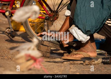 Un uomo anziano lavora a mano affilando coltelli e machete, con una pietra per affilare, al mercato Bai Don di Pakse Foto Stock