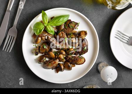 Fegato di pollo fritto con funghi su piatto bianco su fondo di pietra scura. Vista dall'alto, base piatta Foto Stock