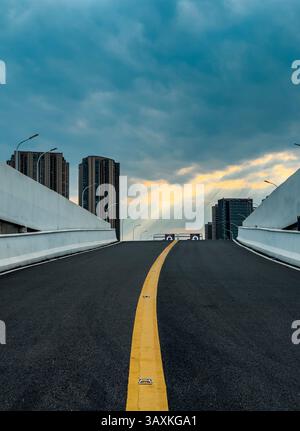 L'ampia autostrada si estende verso un cielo nuvoloso in un ambiente urbano moderno al tramonto Foto Stock