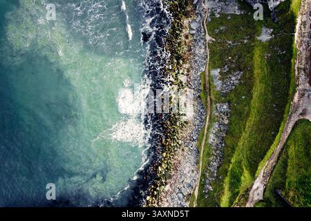 Vista dall'alto del drone sulle onde schiumose che colpiscono le rocce lungo la costa Foto Stock