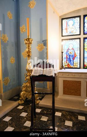 Grodno, Bielorussia, 03.01.2025 Un candelabro d'oro con una candela si trova accanto a una libreria. La camera è decorata con una parete blu e una vetrata colorata Foto Stock