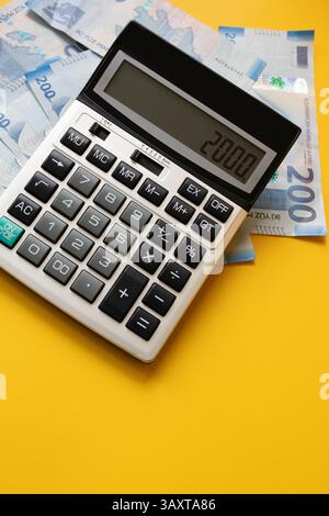 Vista dall'alto di una calcolatrice digitale che mostra il numero 2000, collocata su sfondo giallo accanto alle banconote azere da 200 manat Foto Stock