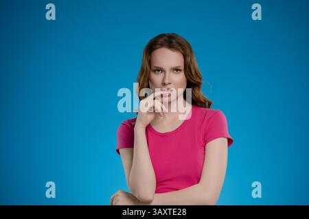 La donna posa in studio con sfondo blu, mostrando una serie di emozioni ed espressioni mentre indossa un vivace top rosa Foto Stock
