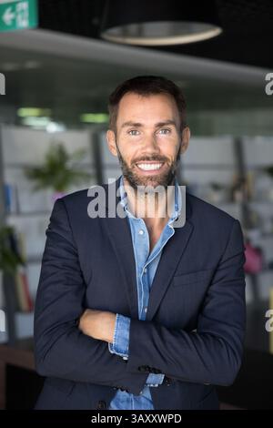 Bellissimo uomo d'affari di mezza età in giacca formale che posa nello spazio di lavoro Foto Stock
