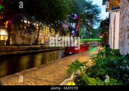 San Antonio, Texas - 4 aprile 2025: Le persone cenano e camminano lungo il famoso lungofiume di San Antonio mentre passano le barche. Foto Stock
