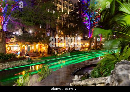 San Antonio, Texas - 4 aprile 2025: Le persone cenano e camminano lungo il famoso lungofiume di San Antonio mentre passano le barche. Foto Stock