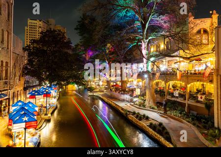 San Antonio, Texas - 4 aprile 2025: Le persone cenano e camminano lungo il famoso lungofiume di San Antonio mentre passano le barche. Foto Stock