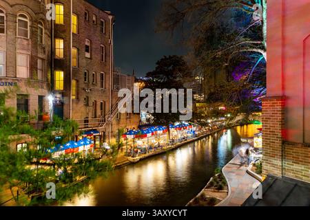 San Antonio, Texas - 4 aprile 2025: Le persone cenano e camminano lungo il famoso lungofiume di San Antonio mentre passano le barche. Foto Stock