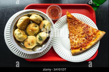 Una fetta di pizza Margherita su un piatto di carta e una porzione di nodi d'aglio in un contenitore di alluminio. Vassoio da portata rosso Foto Stock