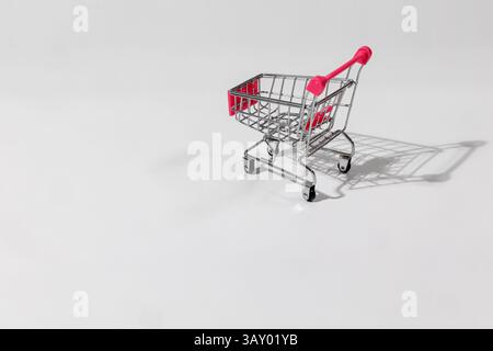 Mini carrello con manico rosa. Piccolo carrello della spesa in metallo con manico rosa su sfondo bianco, che proietta un'ombra sotto l'illuminazione dello studio. Foto Stock