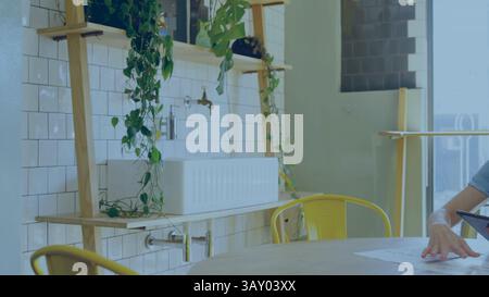 Donna di mezza età che esamina i documenti e utilizza un tablet in un angolo cottura piatto con piante, ufficio Foto Stock