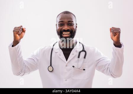 Ritratto di un medico nero felice che sorride e solleva pugno in festa. Studio girato su sfondo grigio. Foto Stock