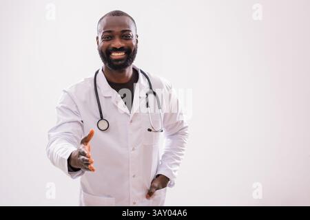 Ritratto di un medico africano fiducioso in uniforme che sta facendo un gesto di stretta di mano su sfondo grigio. Foto Stock