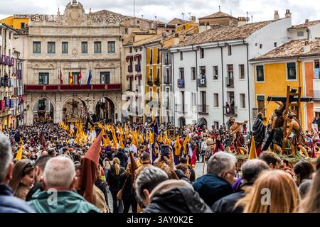 Migliaia di spettatori affollano la Plaza Mayor di Cuenca durante la processione del Venerdì Santo Camino del Calvario, Castilla-La Mancha, Spagna, davanti alla facciata della Casa Consistorial, il municipio (1760-1762, architetto Jaime Bort). Bandiere gialle e viola delle confraternite si ergono sopra la folla, e un gruppo di figure su una scala, che mostra una figura di Cristo sollevata sulla croce, è visibile sullo sfondo. Durante la Semana Santa a Cuenca, 33 Hermandades partecipano a undici processioni attraverso la città durante la Holy Week. Foto Stock