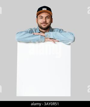 Un uomo sorridente isolato con lo schienale si appoggia su un poster bianco vuoto. Foto Stock