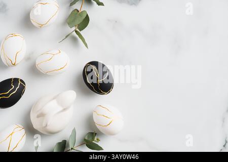 Felice Pasqua piatto composizione laica. Uova di Pasqua di lusso, coniglietto di coniglio, foglie di eucalipto su sfondo marmoreo. Vista dall'alto con spazio per la copia. Foto Stock
