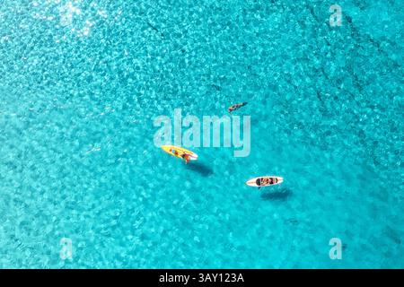 Vista aerea dei kayak nel mare blu al tramonto in estate. Uomo su canoe galleggianti nell'oceano con acqua azzurra trasparente. Isola Sardegna, Italia. Tropicale Foto Stock
