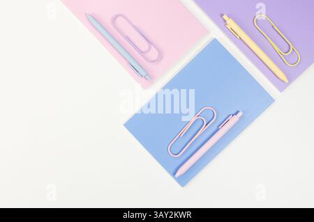 Vista dall'alto dei notebook rosa, viola e blu su sfondo bianco. Penne rosa, gialle e blu, graffette, scuola, carta da parati per ufficio. Flat lay, copia spac Foto Stock