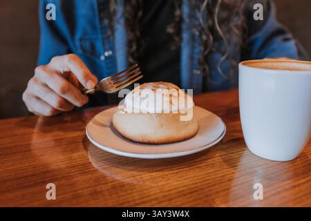 A un uomo piace un rotolo di cannella ricoperto di glassa accanto a una tazza di caffè fumante su un tavolo di legno. Il tavolo crea una calda e invitante colazione atmo Foto Stock