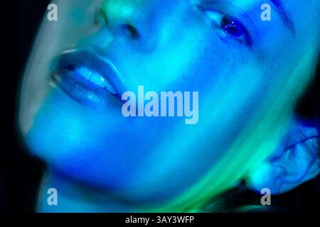 Uno scatto ravvicinato di una donna è bagnato dal viso di una brillante luce blu al neon, che mette in risalto la consistenza e le caratteristiche della pelle. La foto artistica evoca una a futuristica Foto Stock
