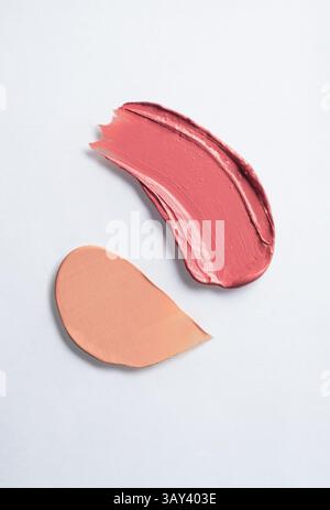Primo piano di bellissimi campioni di trucco rosa e beige spalmati artisticamente su sfondo bianco. Perfetto per presentazioni di bellezza e cura della pelle. Foto Stock