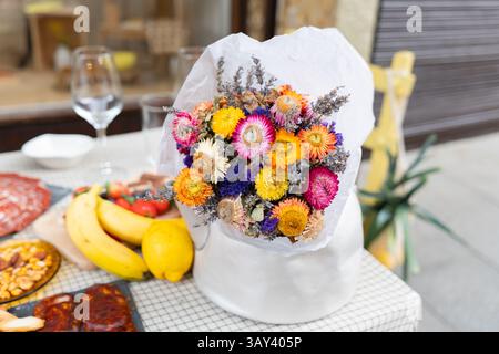 Un vivace bouquet di fiori secchi aggiunge fascino a un tavolo adornato con frutta fresca e prelibatezze. Questa disposizione per le feste dona calore ed eleganza Foto Stock
