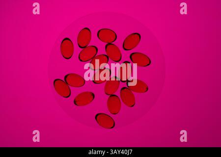 Colorate capsule rosse di omega-3 e vitamina D raggruppate su un vivace sfondo rosa, che enfatizza la salute e la nutrizione. Foto Stock