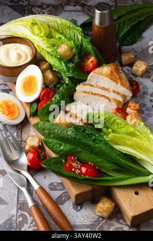 Un'immagine vibrante che mostra gli ingredienti freschi dell'insalata Caesar, tra cui lattuga alla romaina, pollo alla griglia, uova sode, crostini, e pomodori ciliegini, ordinati Foto Stock