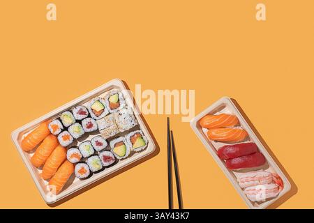 Foto minimalista di scatole da asporto per sushi su sfondo arancione, con rotoli di nigiri e maki con forte illuminazione direzionale Foto Stock
