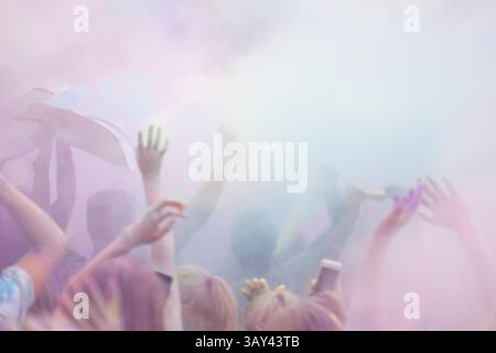 Gruppo di persone corti e irriconoscibili che alzano le mani gioiosamente in mezzo al fumo colorato durante una celebrazione del festival Holi. Foto Stock
