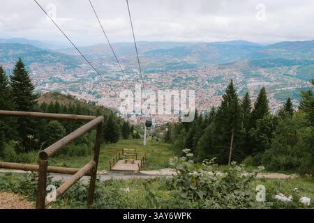 Una vista panoramica di Sarajevo dal monte Trebević, incorniciata da pendii boscosi e dall'iconica funivia che si estende nel cuore di Sarajevp Foto Stock