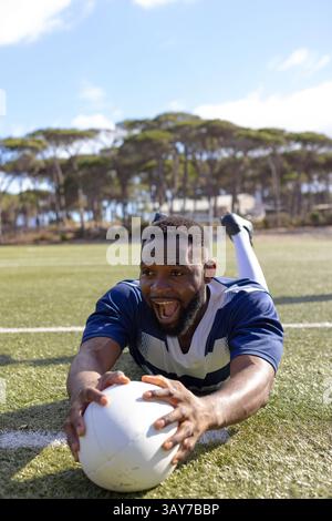 Uomo afroamericano di mezza età disteso su un campo da calcio in erba, che si diverte a giocare a calcio Foto Stock