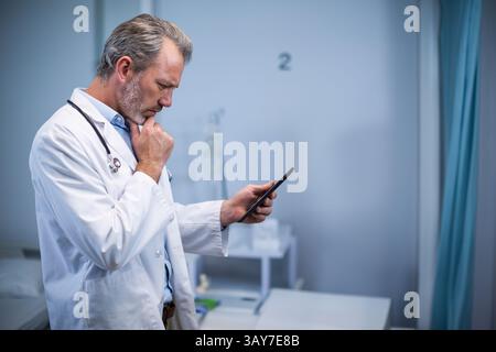 Medico di mezza età che esamina la compressa nella sala esame, indossa lo stetoscopio, supporto IV, spazio di copia Foto Stock