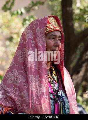 Primo piano di una donna uzbeki anziana che è una ballerina folcloristica che indossa una tunica ikat, un cappello da skullcap ornato e un velo rosa. Fotografato vicino a Baysun, Uzbekistan Foto Stock