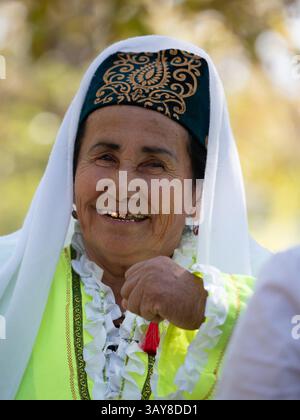 Primo piano di una donna uzbeki sorridente anziana che è una ballerina folcloristica che indossa un costume verde neon, un cappello in velluto e un velo bianco. Baysun, Uzbekistan Foto Stock