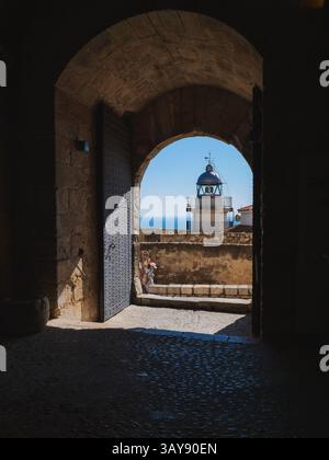 Una vista pittoresca del Faro di Peniscola (Faro de Peniscola) incorniciata da un arcata rustica in pietra, probabilmente all'interno dello storico Castello di Peniscola Foto Stock