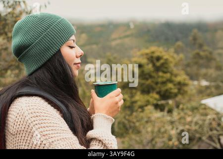 In un momento tranquillo, una donna sorseggia una bevanda rinfrescante all'aperto, completamente circondata da una vegetazione lussureggiante e vibrante Foto Stock