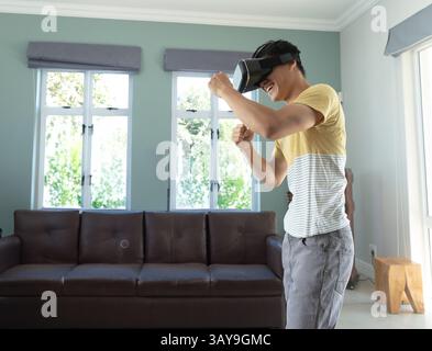 Uomo asiatico che boxe con visore VR in salotto, mostrando realtà virtuale immersiva e spazio di copia Foto Stock