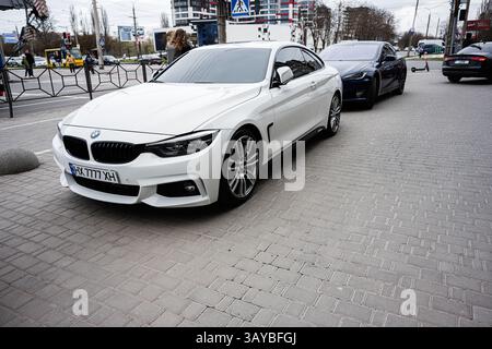 Chmelnytskyi, Ucraina - 16 aprile 2025: Berlina BMW serie 4 bianca parcheggiata su strada urbana con altri veicoli parcheggiati Foto Stock