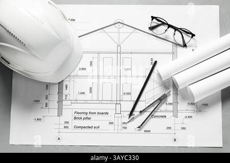 Diversi disegni architettonici, elmetto, matita, divisore e vetri su tavolo grigio, piatto Foto Stock