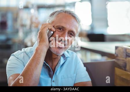 Uomo di mezza età che parla su smartphone in un moderno ambiente da caffè, con una connessione digitale informale Foto Stock