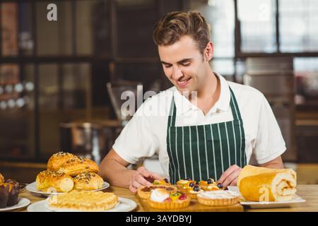 Pasticcere di metà adulto che organizza crostate di frutta su un bancone di legno nella panetteria, con pasticcini Foto Stock