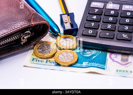 Foto macro di strumenti finanziari britannici, con portafoglio in pelle, monete da sterlina, banconota da 5 libbre, chiavi della calcolatrice, penna metallica e affilatrice blu Foto Stock