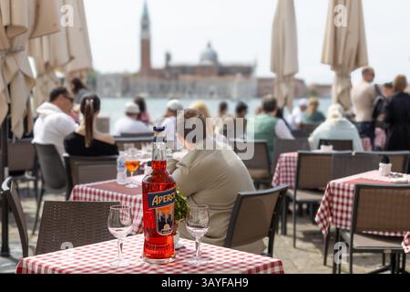 Venezia, Italia - 20 aprile 2025: Bottiglia di Aperol nell'affollata scena di caffè sul lungomare Foto Stock