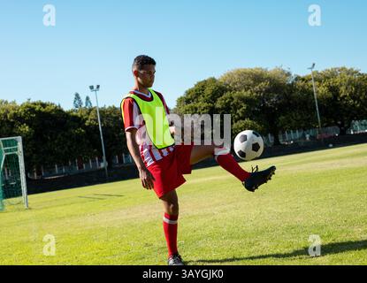 Giocatore di calcio maschile giocolando palla di calcio sul campo da calcio, con pettorina giallo fluorescente, copia spazio Foto Stock