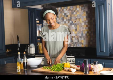 Donna afroamericana che taglia lattuga e funghi sul tagliere dell'isola Kitchen Foto Stock